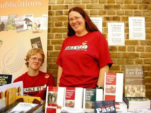 Pippa with her son Blake at the Cable Street bookfair. Pippa standing and her son Blake sitting behind books.